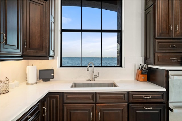 kitchen with dark brown cabinets, a water view, and sink