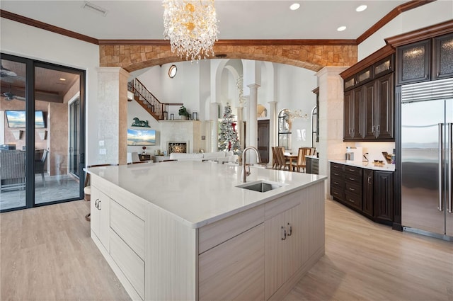 kitchen with stainless steel built in refrigerator, dark brown cabinets, crown molding, sink, and a center island with sink