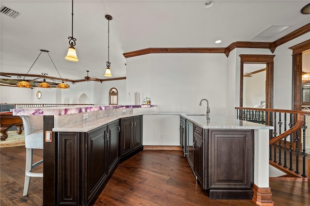 kitchen with dark wood-type flooring, light stone counters, crown molding, pendant lighting, and a breakfast bar area