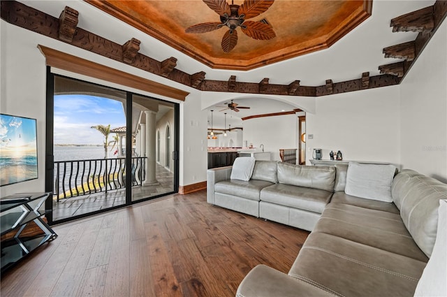 living room featuring ceiling fan, a raised ceiling, and wood-type flooring