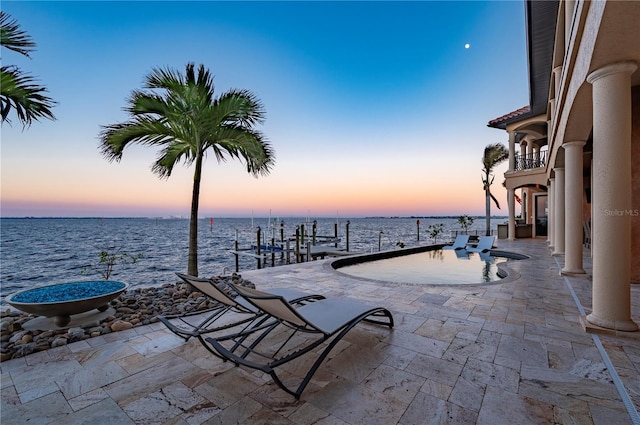 patio terrace at dusk with a balcony, a dock, and a water view