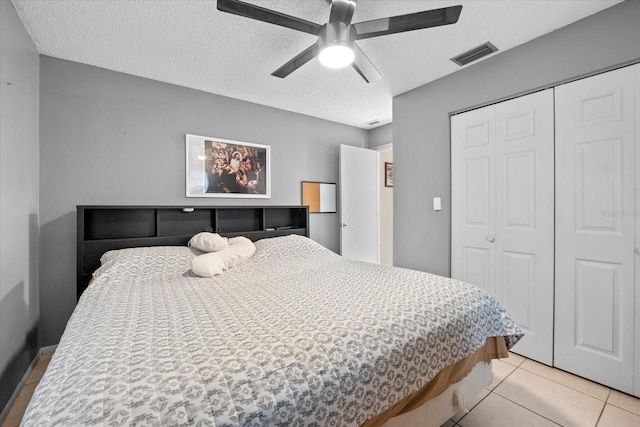 bedroom with ceiling fan, light tile patterned flooring, a textured ceiling, and a closet