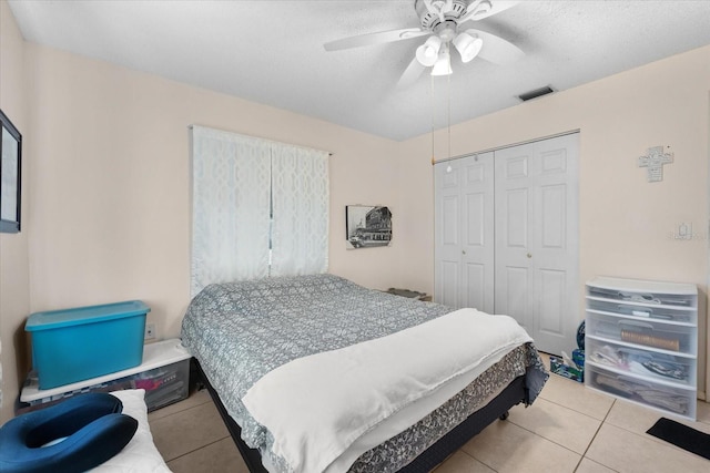 bedroom with ceiling fan, a closet, light tile patterned floors, and a textured ceiling