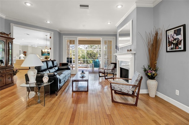 living room with a high end fireplace, light hardwood / wood-style flooring, ceiling fan, and crown molding