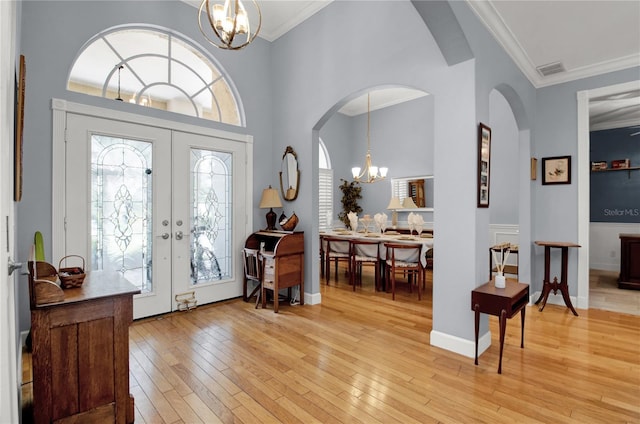 entryway with crown molding, french doors, a chandelier, and light hardwood / wood-style floors