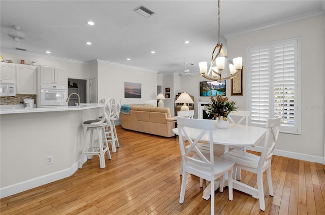 dining space with ornamental molding, sink, and light hardwood / wood-style flooring