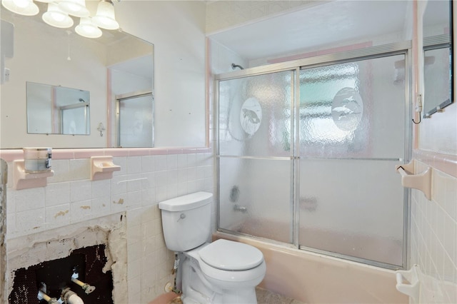 bathroom featuring a fireplace, toilet, shower / bath combination with glass door, and tile walls