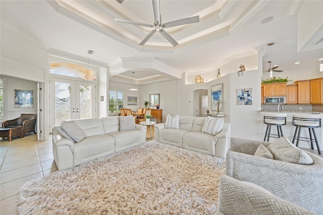 living room featuring french doors, light tile patterned floors, a raised ceiling, ornamental molding, and a ceiling fan