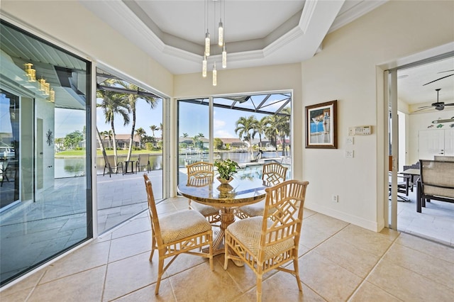 dining space with a water view, ceiling fan, a healthy amount of sunlight, and a tray ceiling