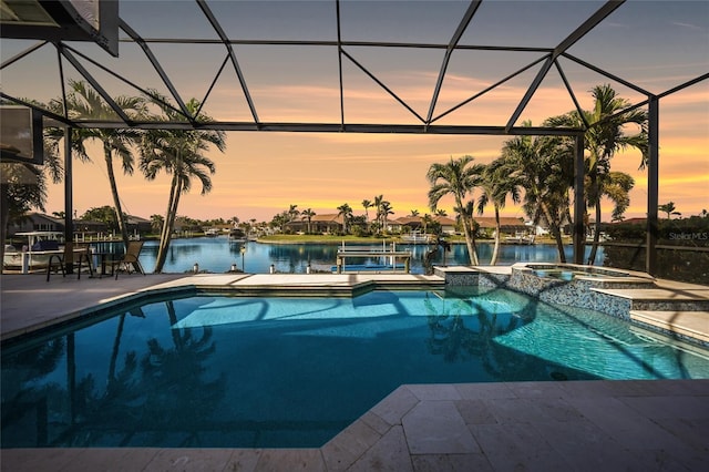 pool at dusk featuring a lanai, a patio area, a water view, and an in ground hot tub