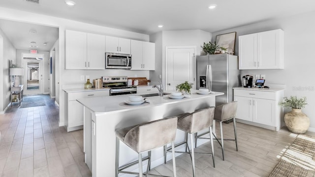 kitchen featuring white cabinetry, stainless steel appliances, light hardwood / wood-style flooring, an island with sink, and a breakfast bar