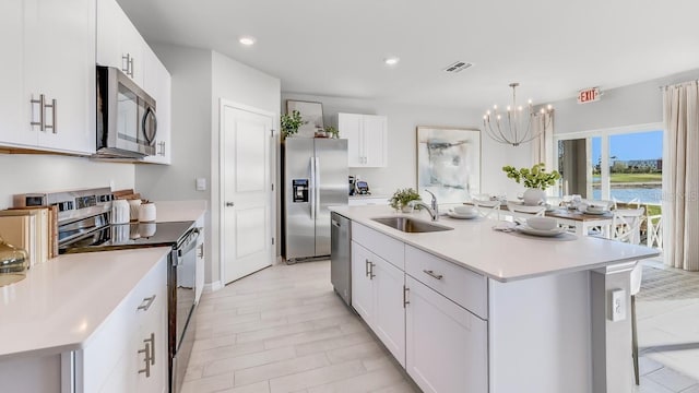 kitchen with appliances with stainless steel finishes, sink, a center island with sink, a notable chandelier, and white cabinetry