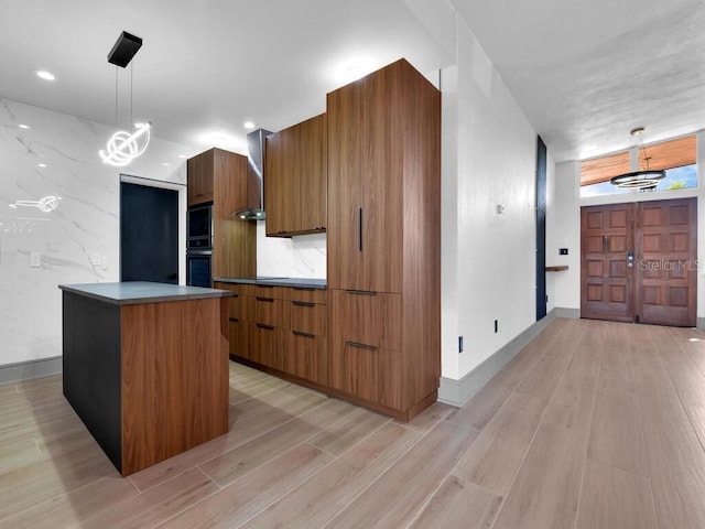 kitchen featuring wall chimney exhaust hood, black double oven, pendant lighting, a center island, and light hardwood / wood-style floors