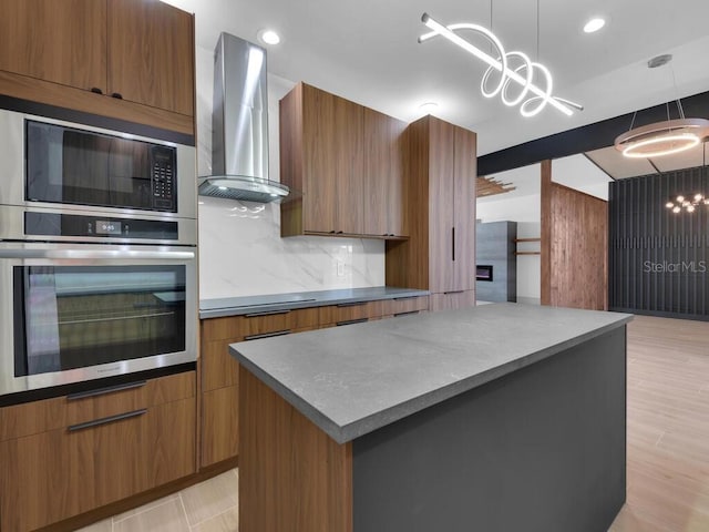 kitchen with appliances with stainless steel finishes, decorative light fixtures, an inviting chandelier, and wall chimney exhaust hood