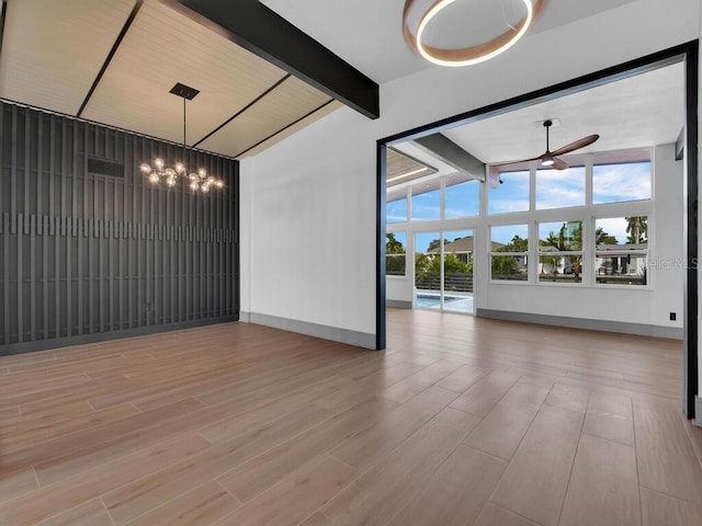 empty room featuring lofted ceiling with beams, light hardwood / wood-style floors, and ceiling fan with notable chandelier