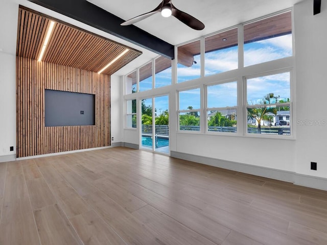 unfurnished living room featuring beam ceiling, light hardwood / wood-style flooring, ceiling fan, and a high ceiling