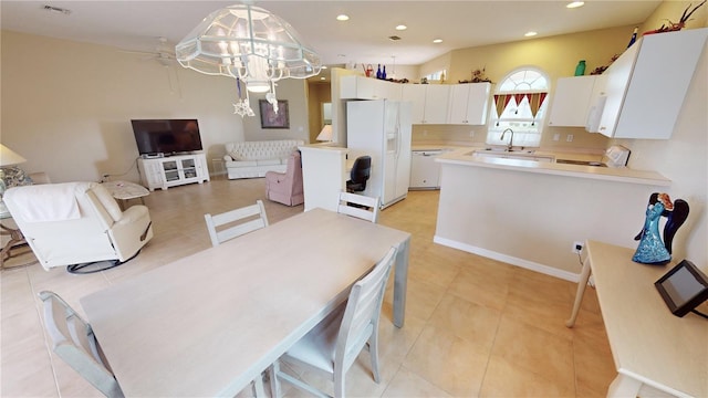 kitchen featuring sink, white fridge with ice dispenser, light tile patterned floors, decorative light fixtures, and white cabinetry