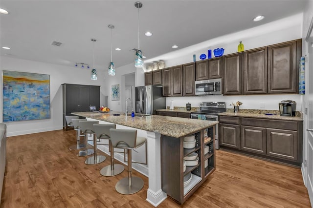 kitchen featuring appliances with stainless steel finishes, hanging light fixtures, an island with sink, and dark brown cabinetry