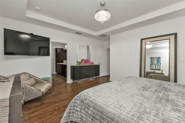 bedroom featuring dark wood-type flooring, ensuite bathroom, an inviting chandelier, and a tray ceiling