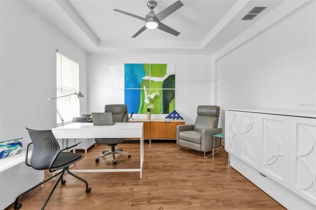 office space with hardwood / wood-style flooring, ceiling fan, and a tray ceiling