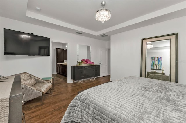 bedroom featuring a raised ceiling, an inviting chandelier, dark hardwood / wood-style flooring, and ensuite bath