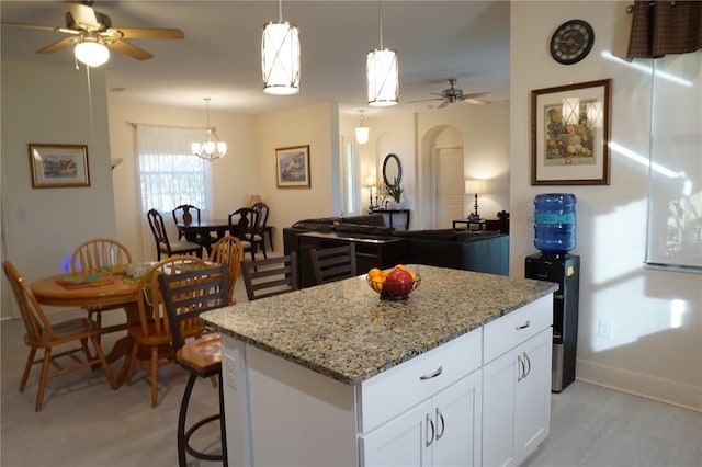 25115 Esmeralda Ct, Punta Gorda, FL 33955 - kitchen with ceiling fan, a kitchen island, light stone countertops, white cabinetry, and pendant lighting