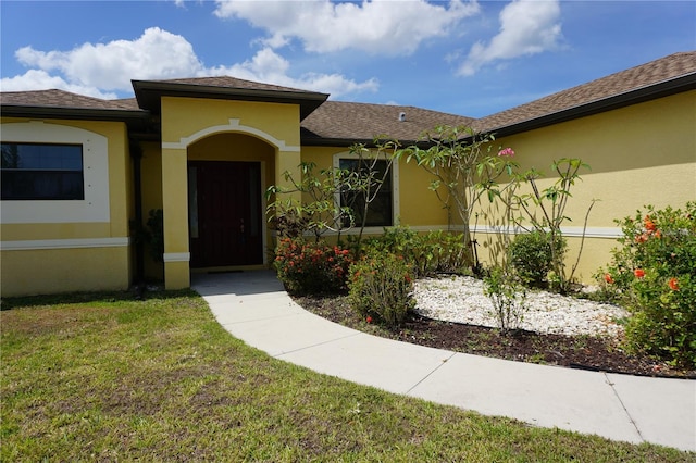 doorway to property with a lawn, a shingled roof, and stucco siding