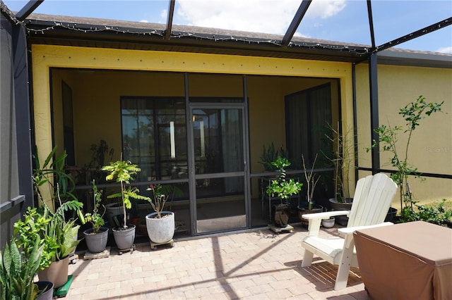 rear view of property featuring a patio, glass enclosure, stucco siding, and a sunroom