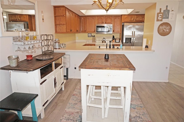 kitchen featuring an inviting chandelier, sink, appliances with stainless steel finishes, light hardwood / wood-style floors, and kitchen peninsula