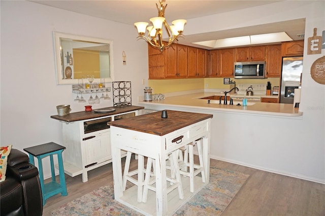 kitchen with sink, wood-type flooring, hanging light fixtures, appliances with stainless steel finishes, and kitchen peninsula