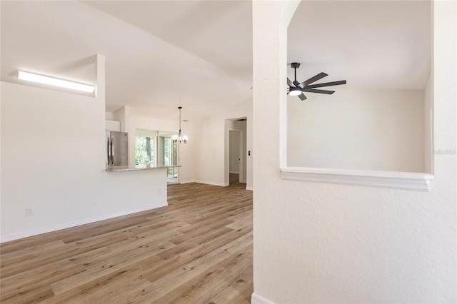 unfurnished living room featuring ceiling fan with notable chandelier, light hardwood / wood-style floors, and lofted ceiling