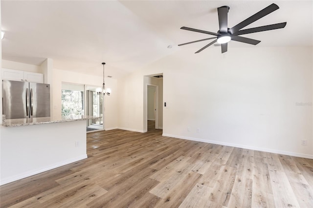 unfurnished living room featuring ceiling fan with notable chandelier, vaulted ceiling, and light hardwood / wood-style flooring