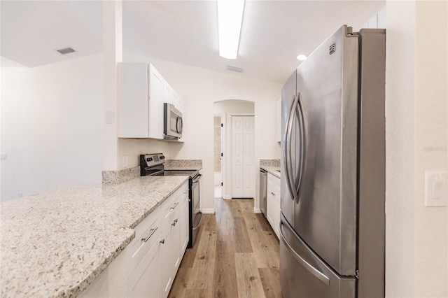 kitchen featuring appliances with stainless steel finishes, light wood-type flooring, white cabinetry, and light stone counters