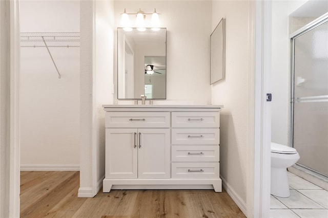 bathroom with vanity, hardwood / wood-style flooring, ceiling fan, toilet, and an enclosed shower