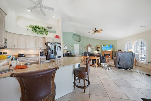 kitchen featuring light stone countertops, stainless steel fridge, a breakfast bar, sink, and light tile patterned floors