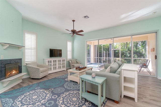 living room with a fireplace, a wealth of natural light, light hardwood / wood-style flooring, and ceiling fan