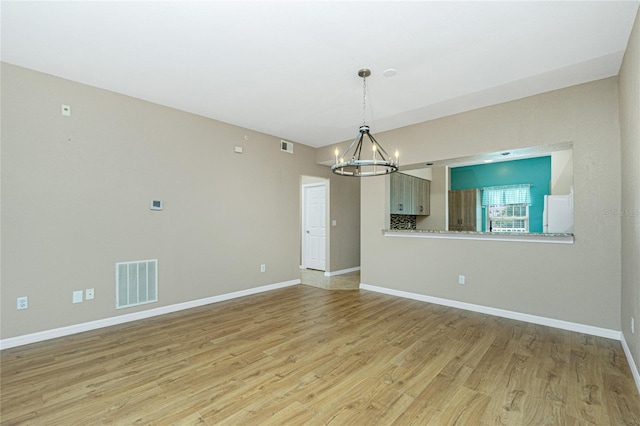 unfurnished room featuring a notable chandelier and light wood-type flooring