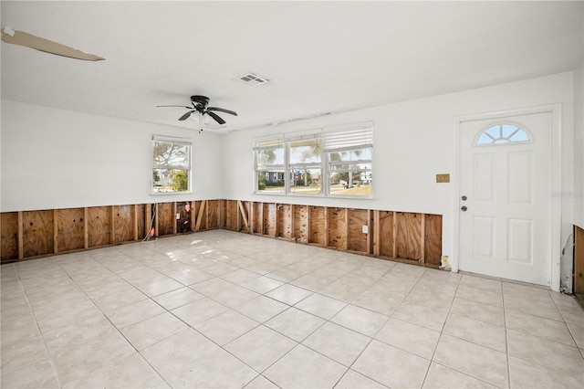 tiled foyer featuring ceiling fan and wood walls