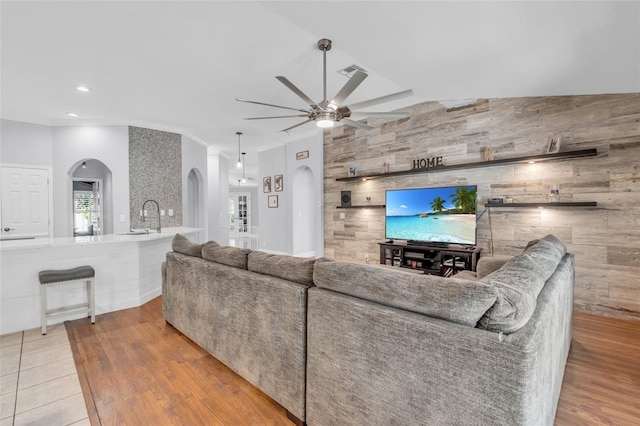 living room with sink, wooden walls, vaulted ceiling, light hardwood / wood-style flooring, and ceiling fan