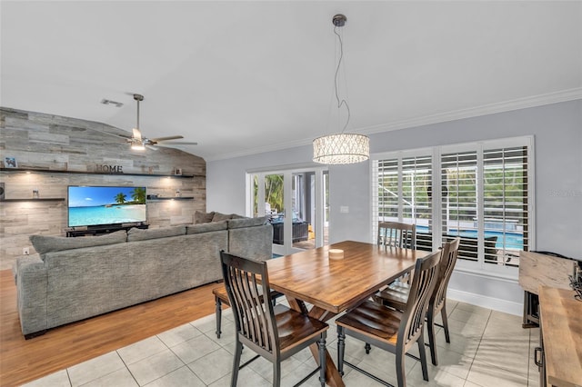 tiled dining room featuring ceiling fan with notable chandelier, vaulted ceiling, ornamental molding, and wood walls