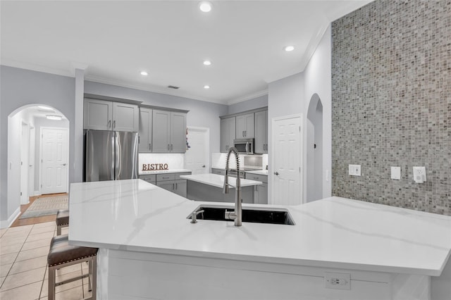 kitchen with sink, backsplash, a breakfast bar, appliances with stainless steel finishes, and ornamental molding