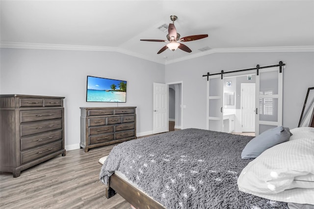 bedroom with light wood-type flooring, ceiling fan, crown molding, a barn door, and connected bathroom