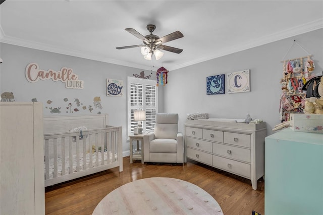 bedroom with hardwood / wood-style flooring, ceiling fan, a crib, and ornamental molding