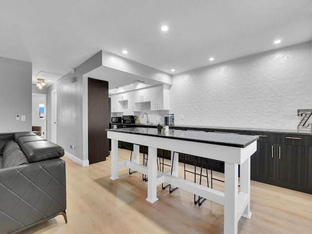 kitchen with sink, a kitchen island, dark brown cabinets, white cabinets, and light wood-type flooring