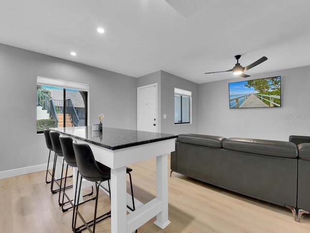 kitchen with dark stone countertops, baseboards, light wood-style flooring, a kitchen breakfast bar, and a center island