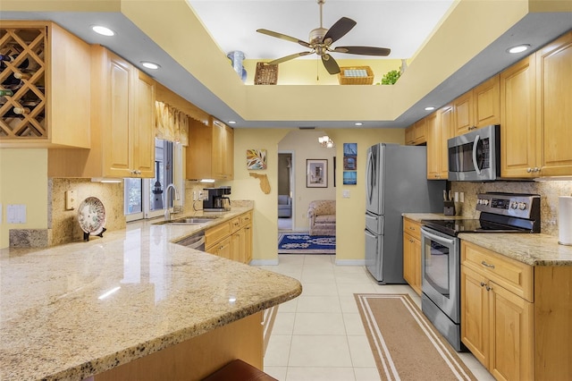 kitchen featuring sink, light tile patterned floors, appliances with stainless steel finishes, light stone counters, and kitchen peninsula