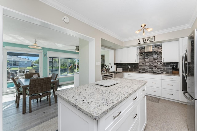 kitchen featuring white cabinets, decorative backsplash, a kitchen island, and wall chimney range hood