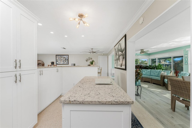 kitchen with light stone countertops, ceiling fan with notable chandelier, white cabinetry, and ornamental molding