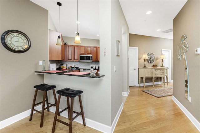 kitchen featuring light hardwood / wood-style flooring, kitchen peninsula, pendant lighting, a kitchen bar, and appliances with stainless steel finishes