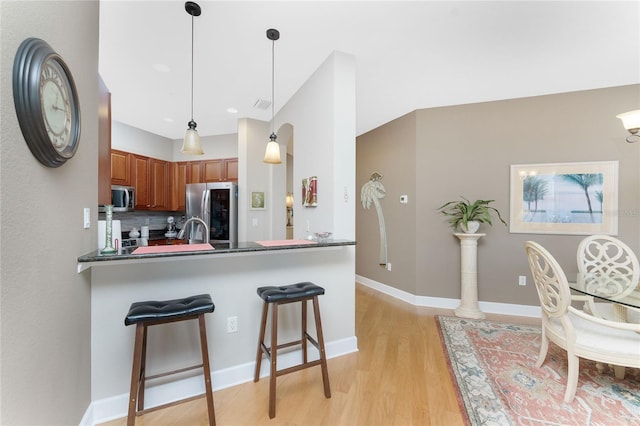 kitchen with kitchen peninsula, appliances with stainless steel finishes, backsplash, a breakfast bar, and pendant lighting